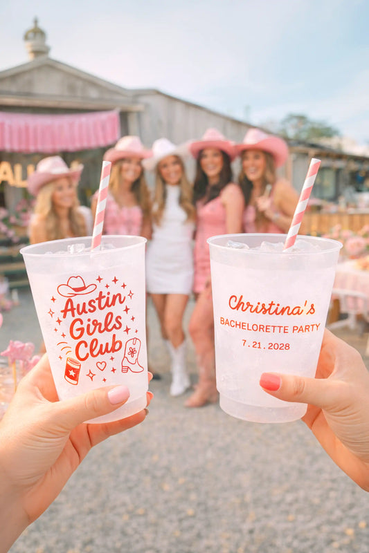 Two hands holding personalized plastic cups with a bachelorette party theme.