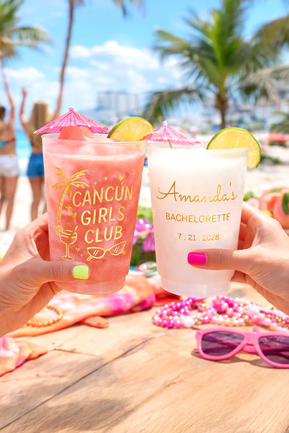 Two cocktails with decorative straws and lime slices, held by hands on a beach setting.