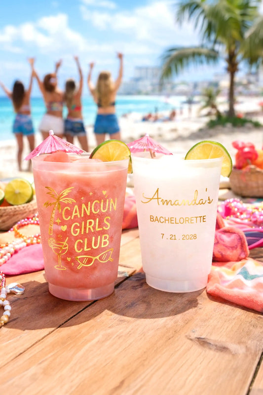 Two pink drinks with decorative straws on a wooden surface with a beach and people in the background.