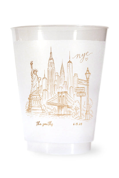 white shatterproof plastic cup on a white background. the cup is printed with a hand drawn illustration of the new york city sklyine with the bride and grooms names and wedding date in gold ink.