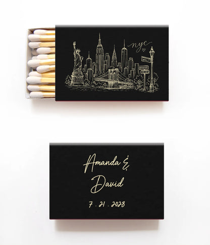 Two black personalized matchboxes on a white background. The top matchbox is open, showing white matches with gold tips and a gold New York City skyline illustration with 'nyc' script.