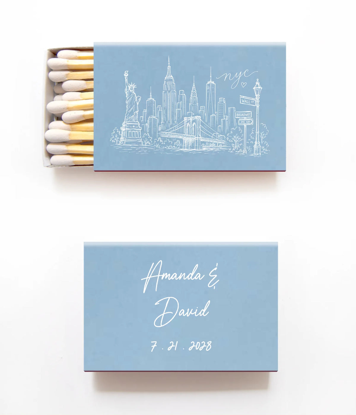 A personalized matchbox set on a clean white background, featuring a light blue cover with a white New York City skyline illustration on the top matchbox and white script names and date on the bottom matchbox.