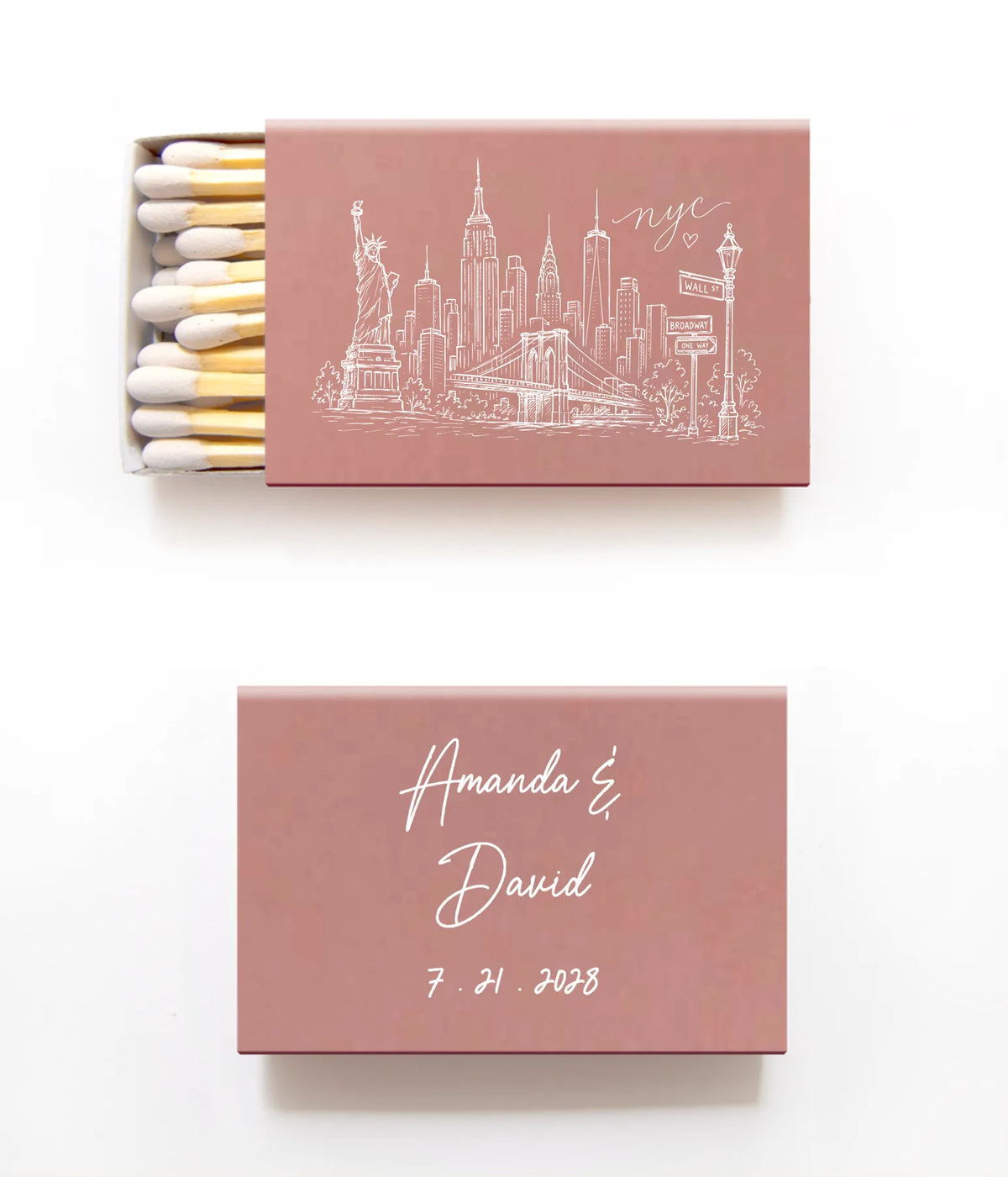 Two dusty rose matchboxes on a white background, one open showing white and gold matches with a white New York City skyline illustration, and one closed with the names 'Amanda & David' and the date '7.21.