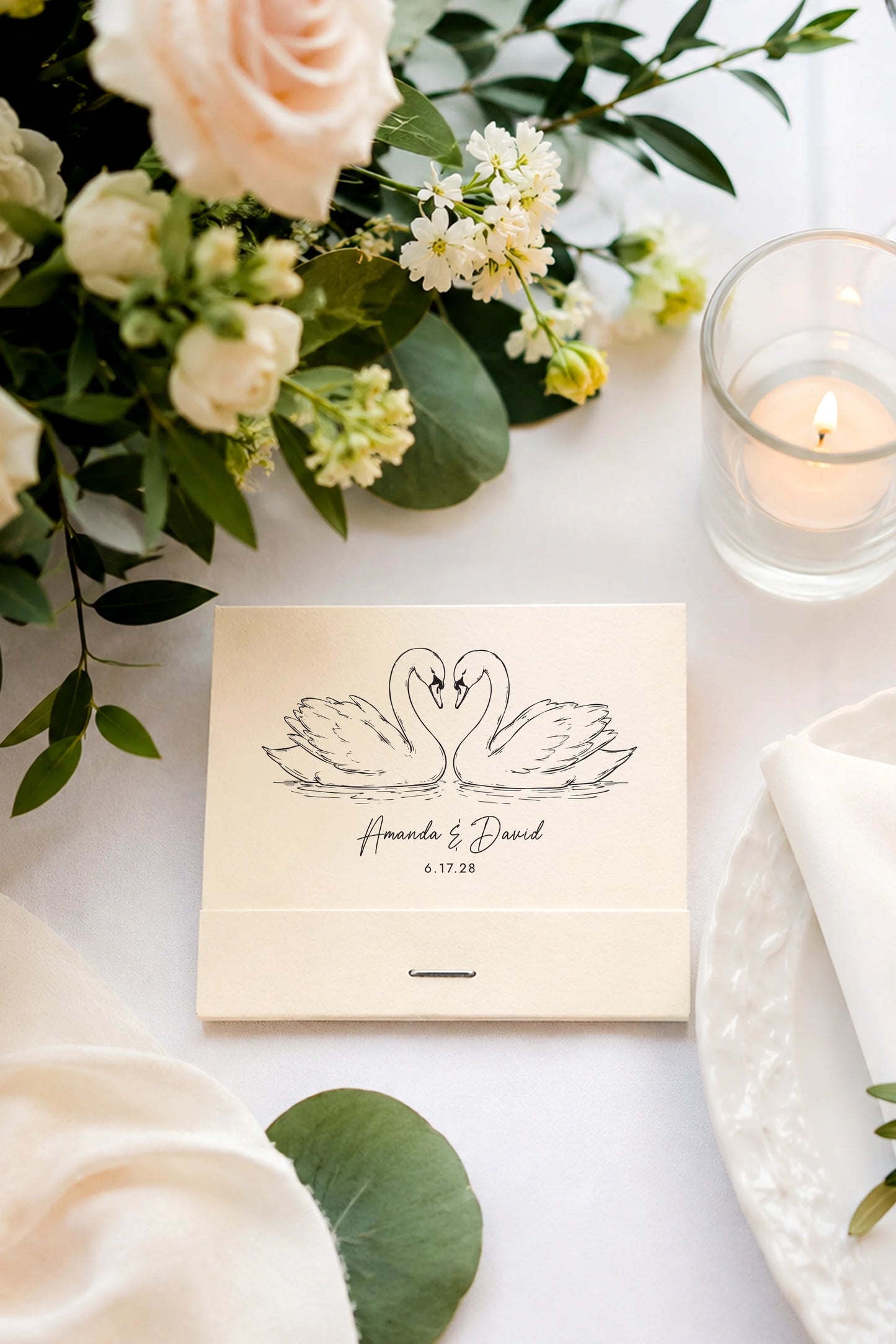 ivory wedding matchbook with swan design on a table with flowers and a candle