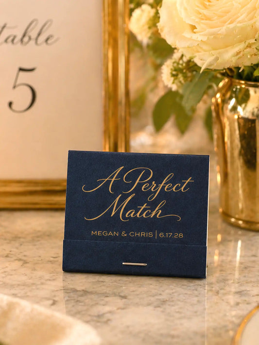 Navy card with gold text 'A Perfect Match' on a marble surface with flowers in the background