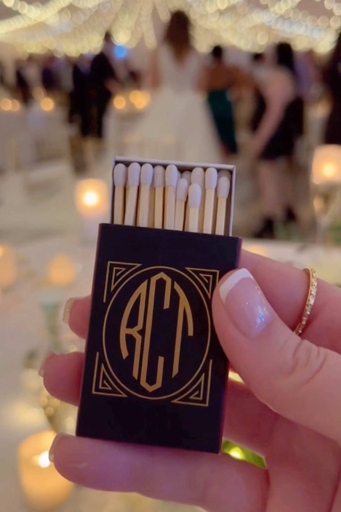 Matchbook with initials held by a hand against a blurred wedding background