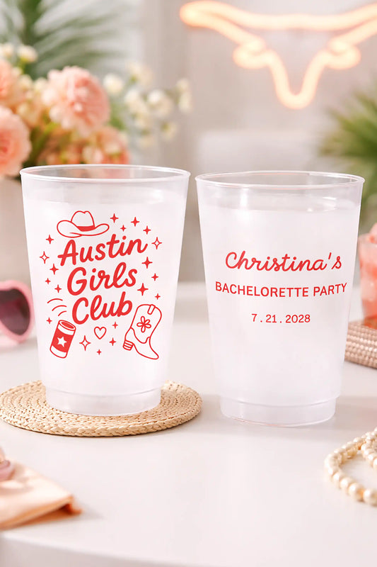 Two clear plastic bachelorette party cups with red Austin Girls Club text and graphics on a white surface, surrounded by cowboy hat, beer and cowboy boots  graphic elements.
