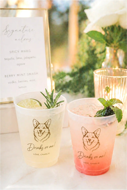 Two colorful drinks in cups with corgi dog illustrations and text, set against a blurred outdoor background.