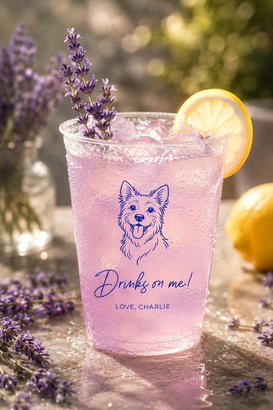 Pink drink in a clear cup with a terrier dog illustration and Drinks on Me text, surrounded by lavender and lemons.