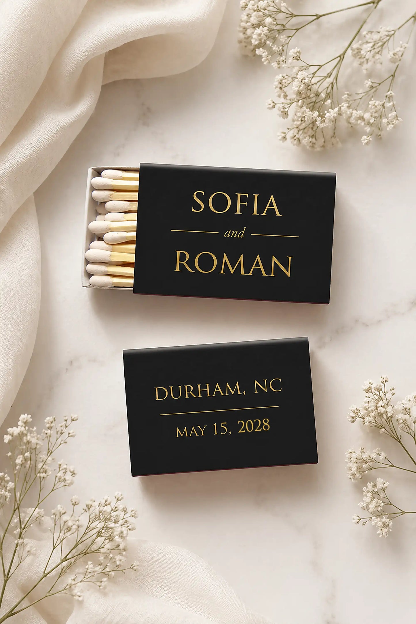 Two black matchboxes with personalized text on a light background with white flowers.