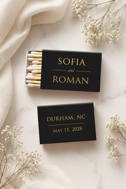Two black matchboxes with personalized text on a light background with white flowers.