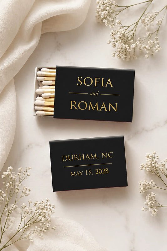 Two black matchboxes with personalized text on a light background with white flowers.