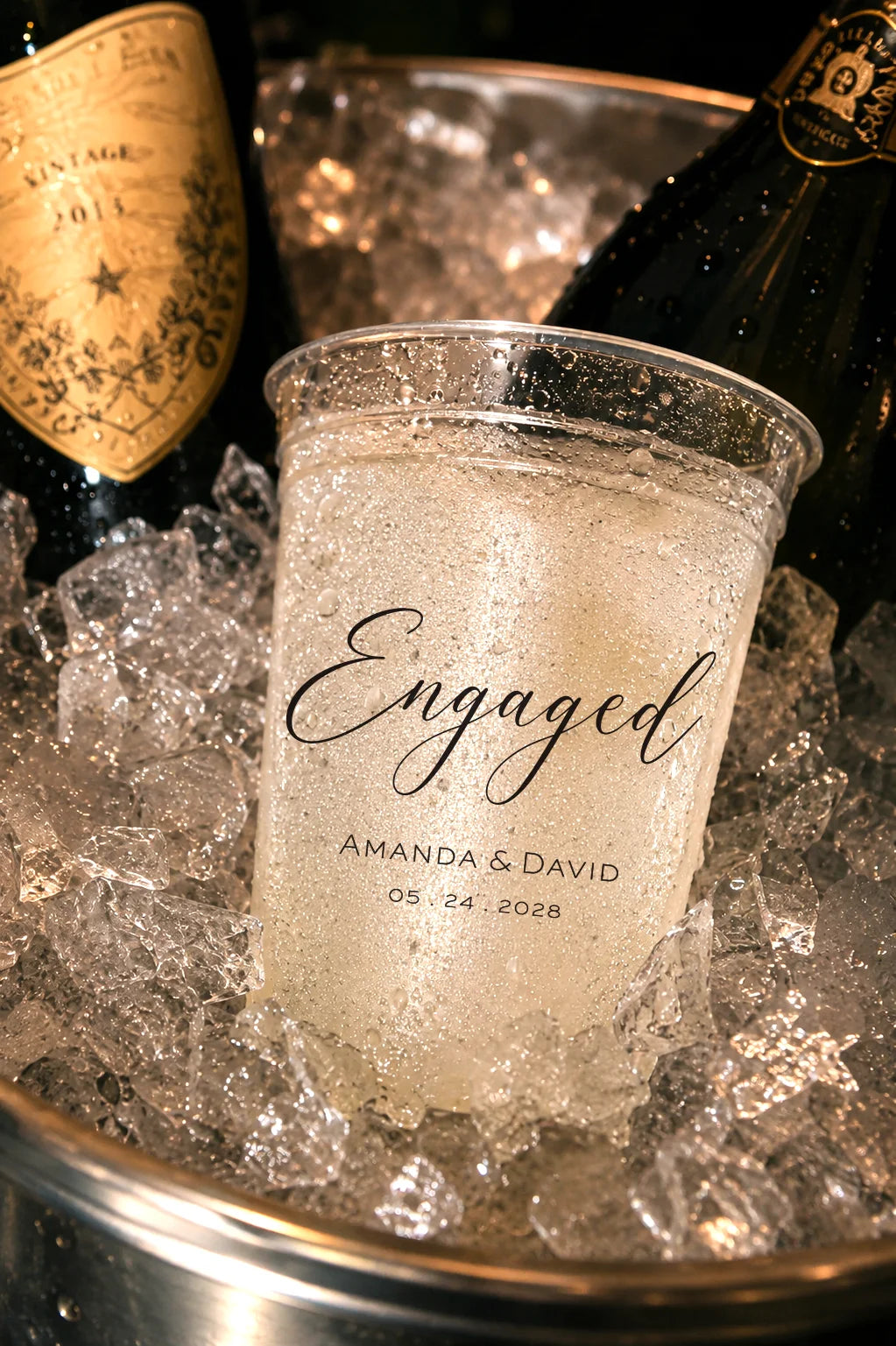 Ice bucket with 'Engaged' personalized glass, surrounded by champagne bottles on ice.
