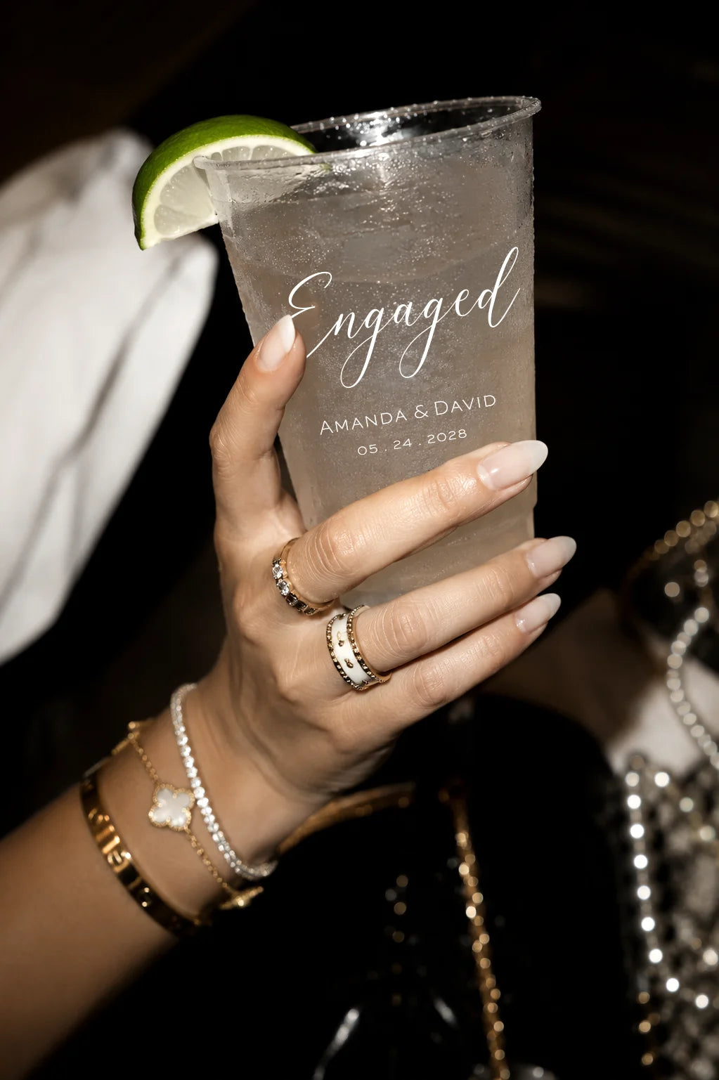 Hand holding a clear plastic cup with 'Engaged' text and a lime wedge, against a dark background.