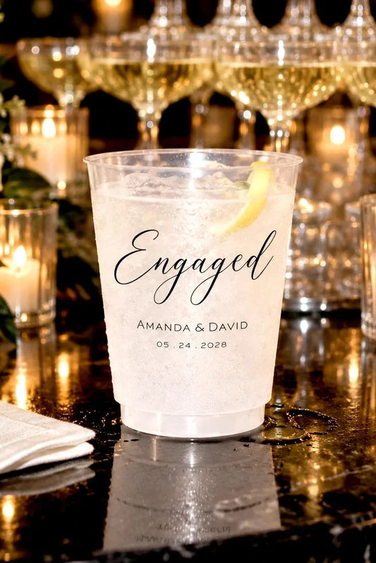 Personalized frosted engagement party cup with names and date on a candlelit champagne bar