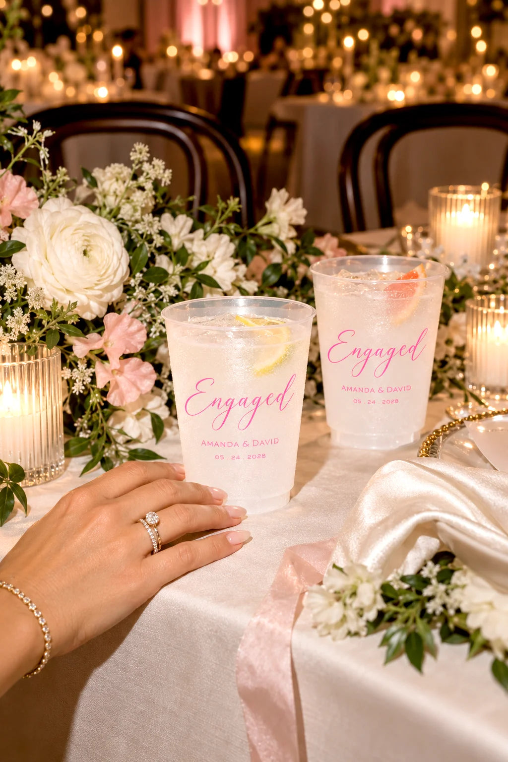 Personalized frosted engagement party cups with custom names and date on an elegant candlelit reception table with flowers
