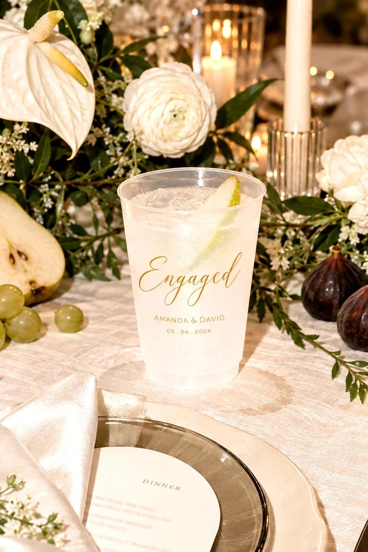 Personalized frosted engagement party cup with custom names and date at an elegant floral dinner table setting
