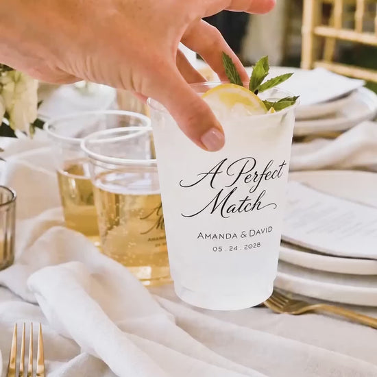 a hand placing on a white wedding table a cup that says a perfect match 
