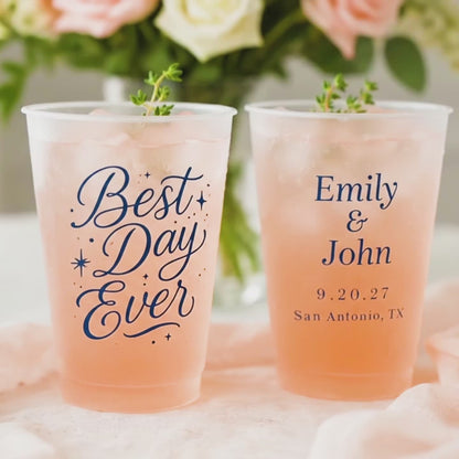 Best Day Ever Wedding Cups with orange drink and thyme garnish on a white and peach table with roses in the background. the 2nd cup says in blue ink, Emily & John, 9.20.27, San Antonio, TX.
