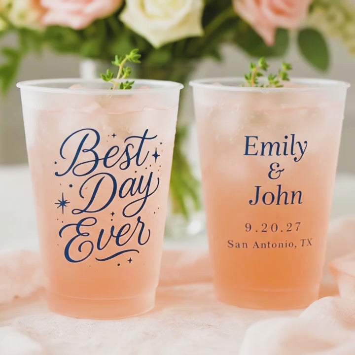Best Day Ever Wedding Cups with orange drink and thyme garnish on a white and peach table with roses in the background. the 2nd cup says in blue ink, Emily & John, 9.20.27, San Antonio, TX.