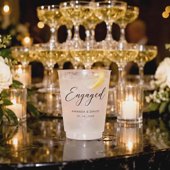 Video of a personalized frosted engagement party cup with custom names and date displayed at a candlelit champagne bar