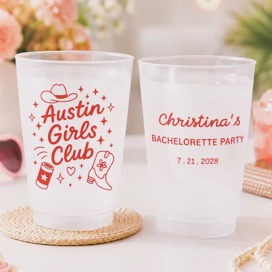 2 customized Shatterproof white cups that say Austin Girls club with graphics on a white party table with pink flowers. 