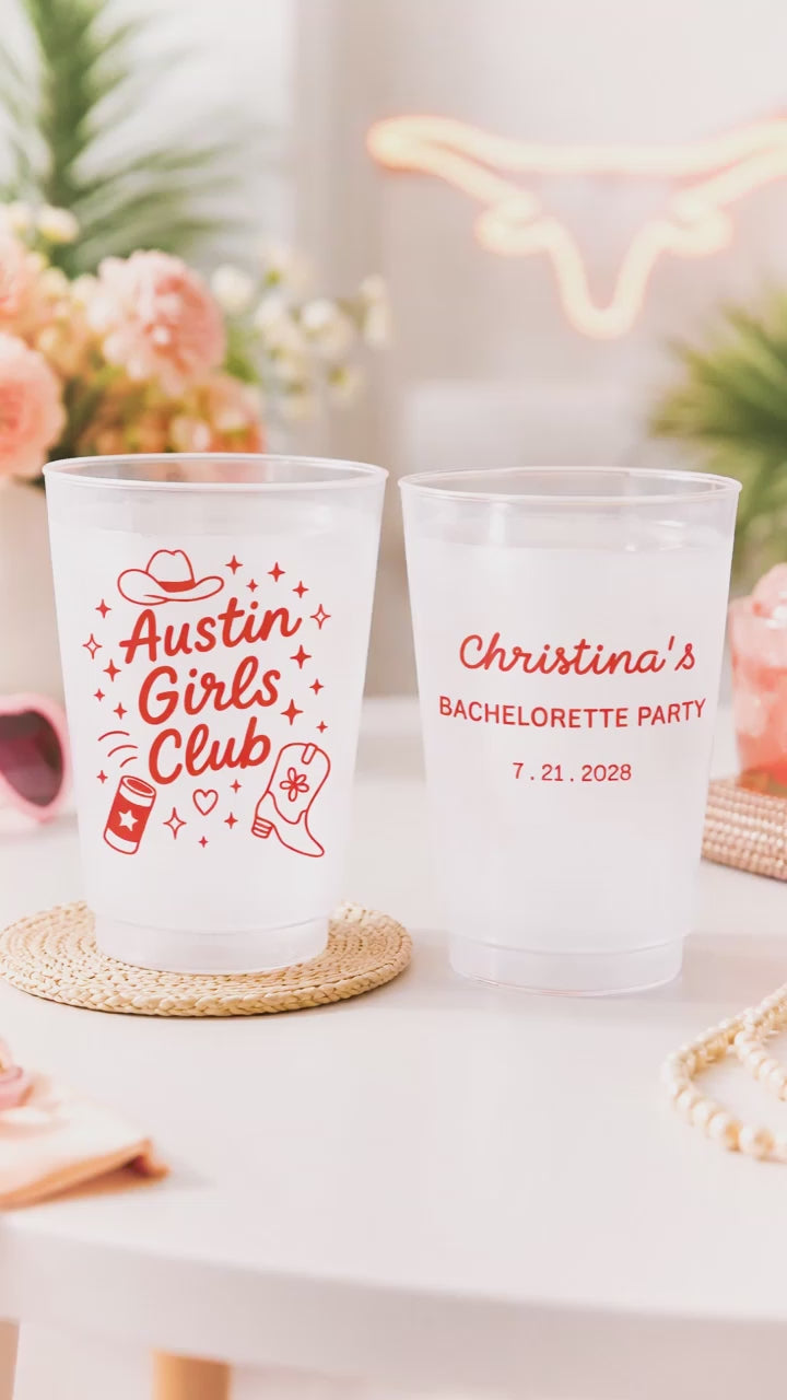 2 customized Shatterproof white cups that say Austin Girls club with graphics on a white party table with pink flowers. 
