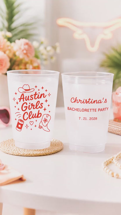 2 customized Shatterproof white cups that say Austin Girls club with graphics on a white party table with pink flowers. 