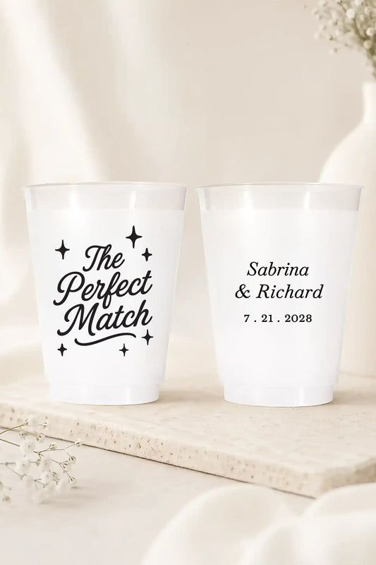 two shatterproof plastic wedding cups that say the perfect match with bride and grooms names and wedding date in black on a white wedding table